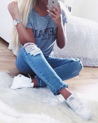 graues bedrucktes T-Shirt mit einem Rundhalsausschnitt, blaue enge Jeans mit Destroyed-Effekten, weiße hohe Sneakers, silberne Uhr für Damen